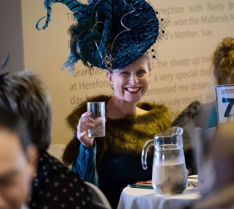 A race goer in a beautiful hat holding a glass in hospitality at Hereford Racecourse.