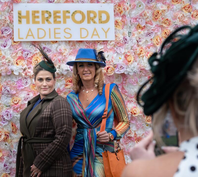 Two ladies posing in front of the flower wall at Hereford Racecourse